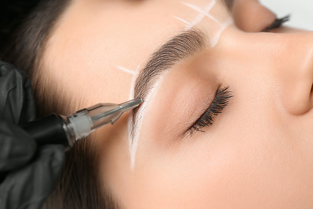 Permanent Make-up Behandlung: Eine Hand mit schwarzem Handschuh führt einen Pigmentierstift mit feiner Nadelkartusche an einer Augenbraue, die vorher mit weißen Linien vorgezeichnet wurde